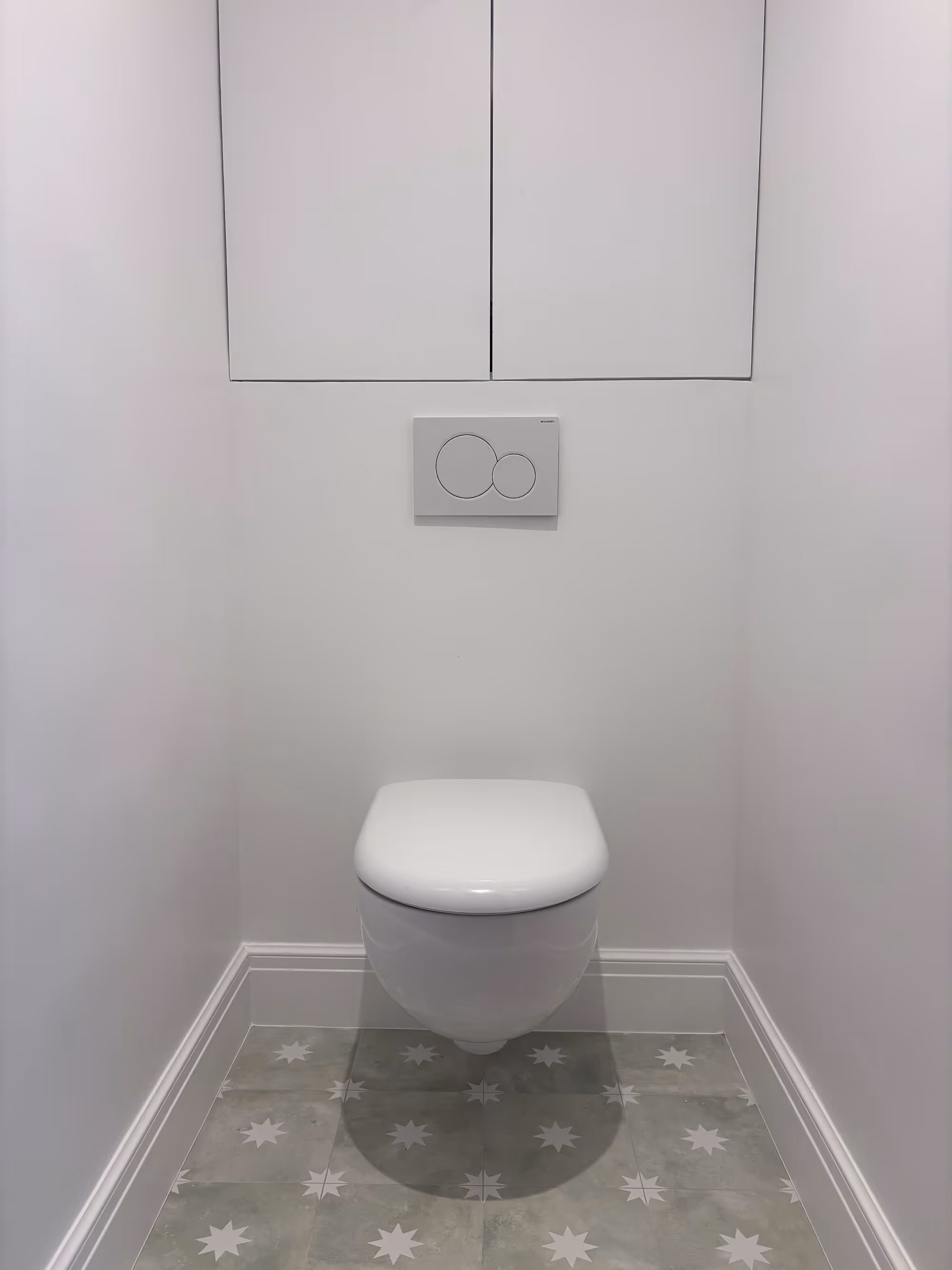 Rénovation d'un appartement haussmannien parisien (5e arr.) : toilettes avec WC suspendu, placard encastré blanc, plaque de chasse double touche et carrelage au sol à motifs étoiles. Réalisation : Aude Riou, architecte d'intérieur.