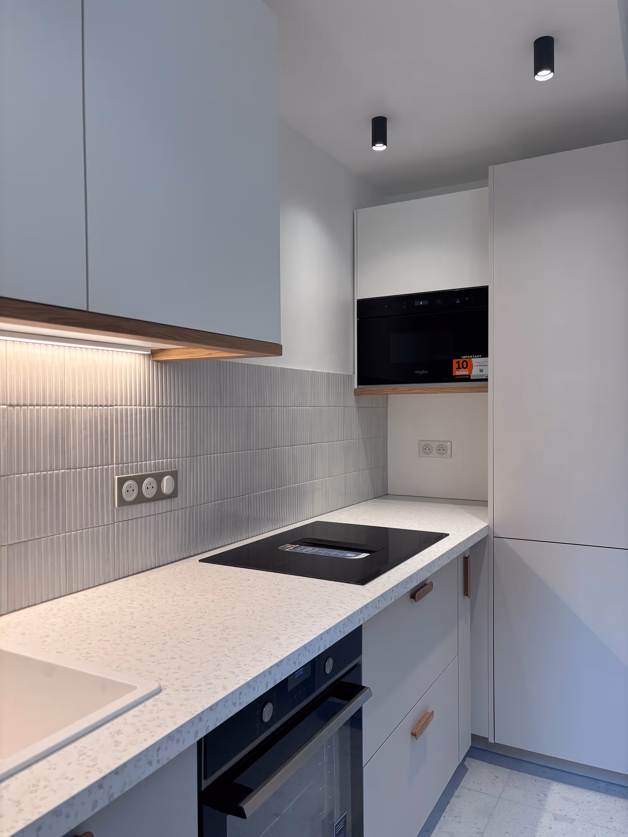 Rénovation d'un appartement haussmannien parisien (5e arr.) : cuisine avec placards blancs, plan de travail granité, four encastré noir, plaque de cuisson, micro-ondes et éclairage sous-meuble. Réalisation : Aude Riou, architecte d'intérieur.
