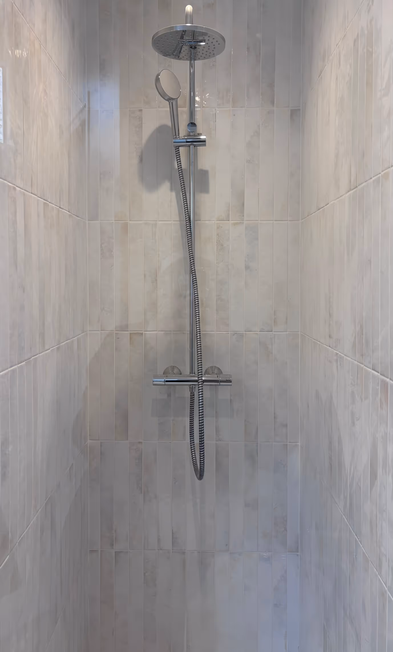 Rénovation d'un appartement haussmannien parisien (5e arr.) : douche à l'italienne avec colonne de douche chromée, pommeau de tête rond et carrelage beige en format vertical. Réalisation : Aude Riou, architecte d'intérieur.