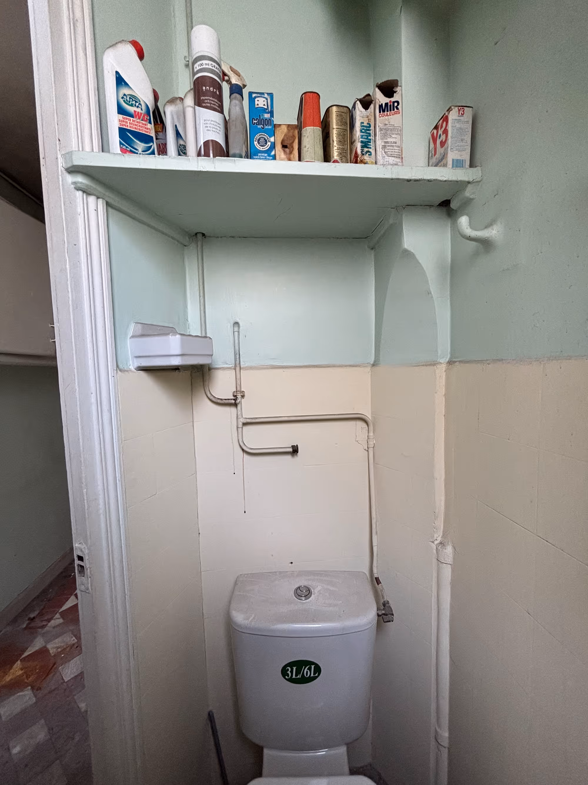 Appartement haussmannien parisien (5e arr.) avant rénovation : toilettes vétustes avec WC à réservoir apparent, tuyauteries apparentes et étagère murale.