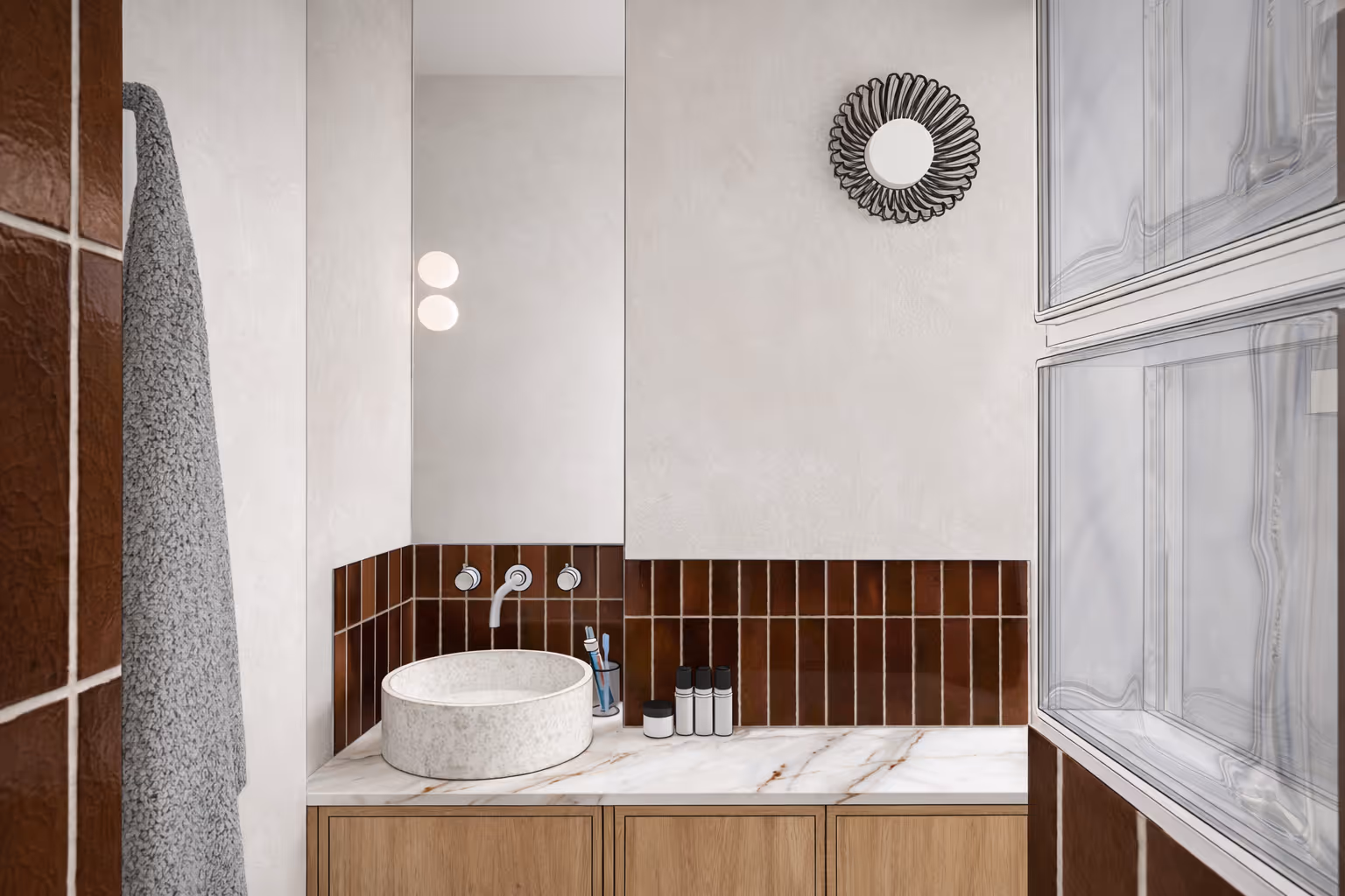 Salle de bain d'un studio parisien : vasque ronde en pierre, plan de travail en marbre, crédence en carrelage marron et meuble de rangement en bois. Réalisation : Aude Riou, architecte d'intérieur.