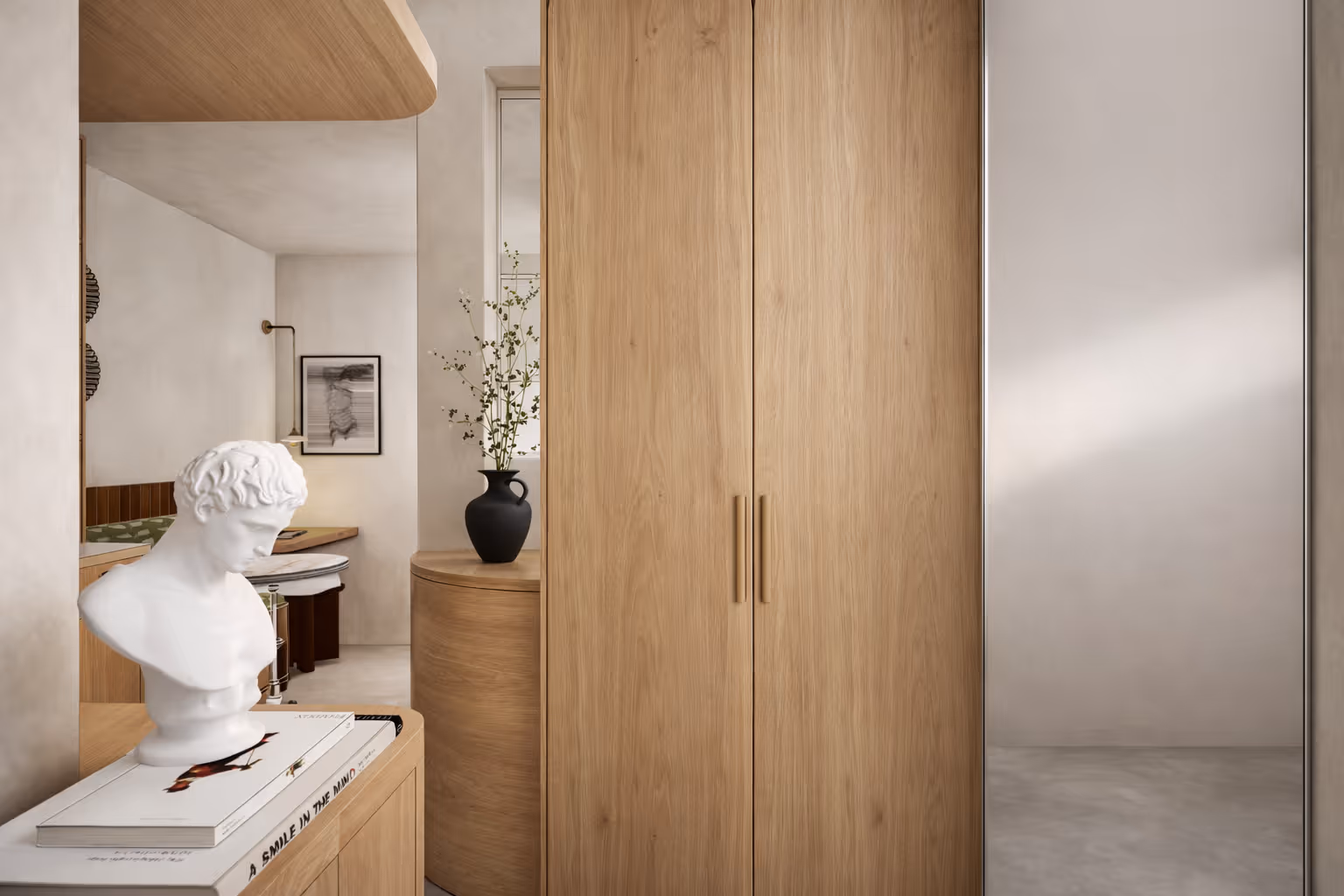 Intérieur moderne d'un studio parisien : armoire en bois, buste blanc posé sur des livres, vase noir avec branches et décoration minimaliste. Réalisation : Aude Riou, architecte d'intérieur.